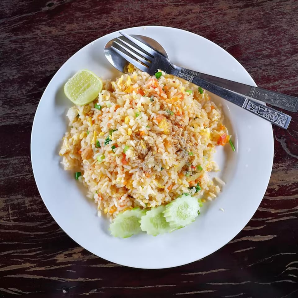 A plate of Jin's Buffet fried rice with lime and cucumber, served with a fork and spoon.