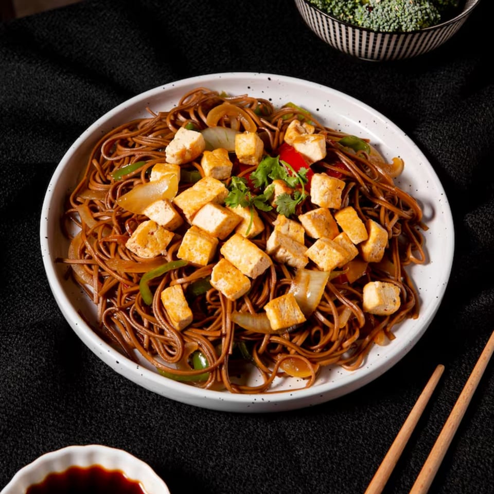 A white bowl of Jin's Buffet's Chinese noodles with tofu, onions, peppers, and cilantro.