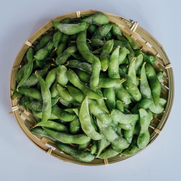 A bamboo basket filled with fresh, green edamame pods, ready to be served at Jin's Buffet.