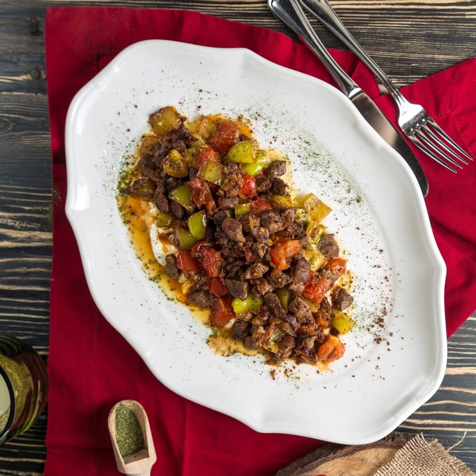 Overhead view of stir-fried beef with green peppers and tomatoes on a white plate.