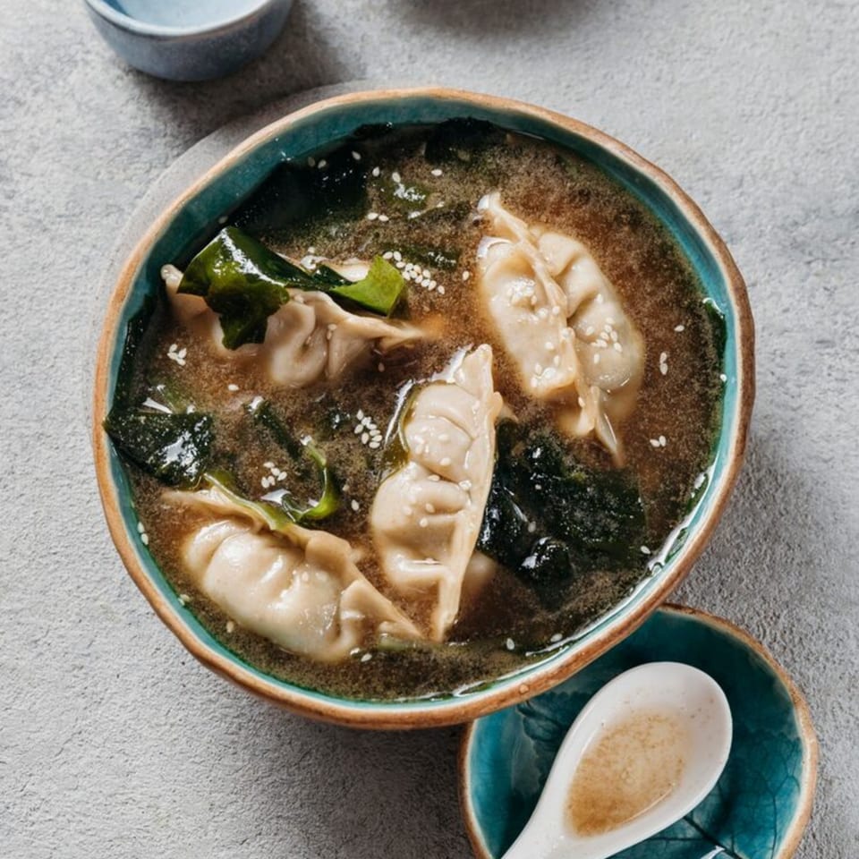 A bowl of Jin's Buffet wonton soup with seaweed and sesame seeds, next to a white spoon.